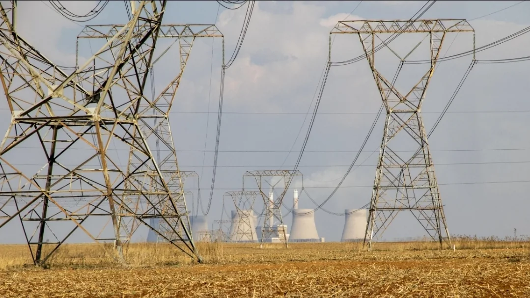 High-voltage pylons crossing a dry field, with power-station cooling towers behind